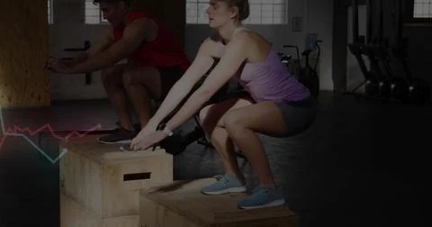 Jumping partners performing box-step squats in garage gym, purple tank and red Stock Photos