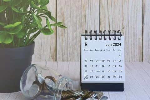 June 2024 desk calendar with stack of coins and potted plant on wooden desk. Stock Photos