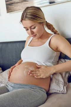 Junge schwangere Frau cremt ihren Bauch ein Young pregnant woman rubbing m... Stock Photos
