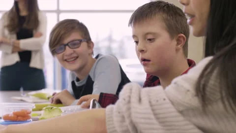 Junior high boy with Down Syndrome eating lunch with friends in school cafeteria Stock Footage 220945452