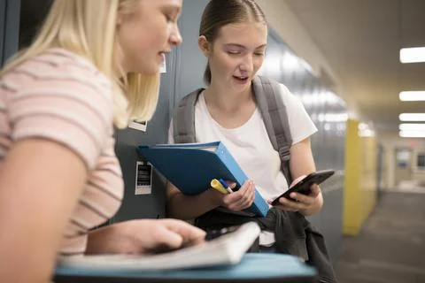 Junior high girl students using smart phone at lockers in corridor Stock Photos