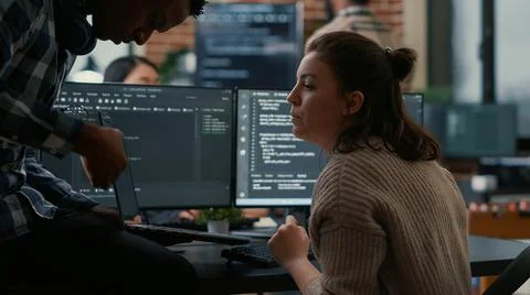Junior programer sitting down on desk showing laptop with source code to senior Stock Photos