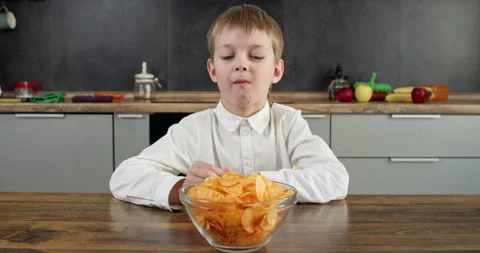 Junior schoolboy eats potato chips from bowl with thumbs up 動画素材 314720254