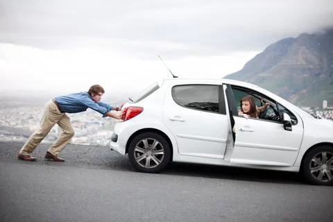 Just keep pushing...Young man pushing the car while his wife tries to start it - Stock Photos