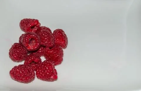 Just red raspberries in a small pile on a white plate. Location on the side. Stock Photos