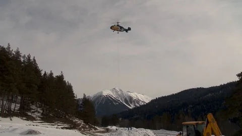 Ka-32 lowers vertically with hopper on background of snow-capped peaks. Stock Footage 106857259