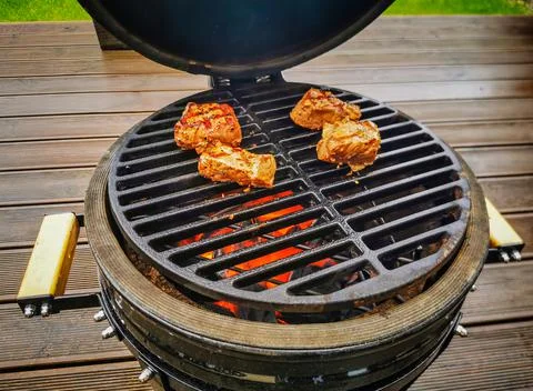 A kamado type barbeque grill with beef steaks roasting on an open fire Фото
