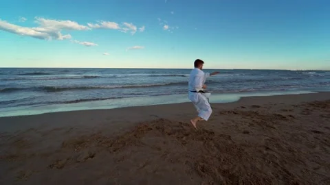 Karate fighter practicing a kata on the beach at sunset. Karate fighter pract Stock Footage 146604854