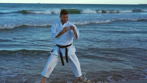 Karate fighter practicing technique on the seashore with his feet in the wate Video stock 146604895