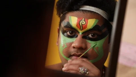 Kathakali dancer looking in the mirror and applying green colour on his face.  Stock Footage 125355698