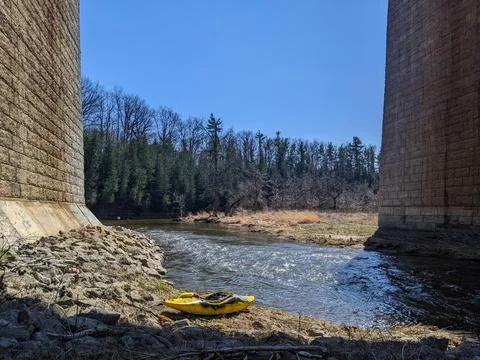 A kayak sits on the side of a river in between two massive pillars from a bridge Stock-Fotos