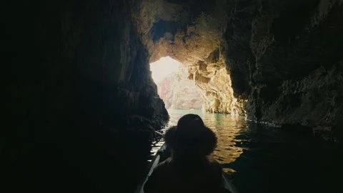 A kayaker in a hat glides through a dark sea cave toward a bright mouth, with Stock Footage 329411560