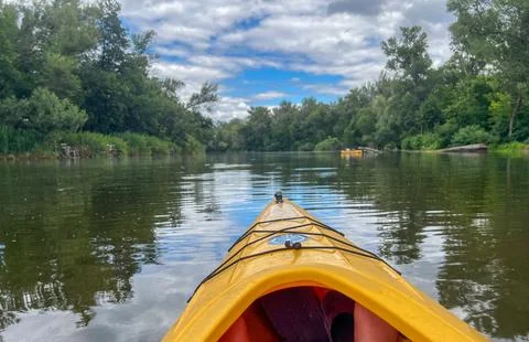 Kayaking on calm river under cloudy sky with lush green trees Stock Photos
