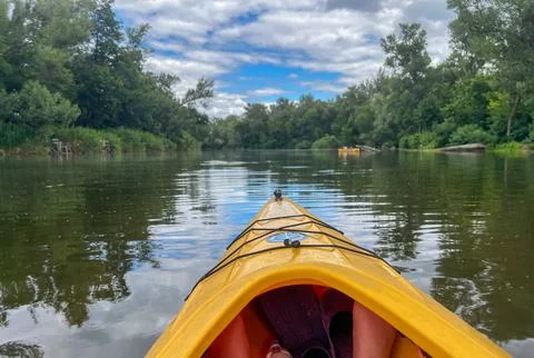 Kayaking on calm river under cloudy sky with lush green trees Stock Photos