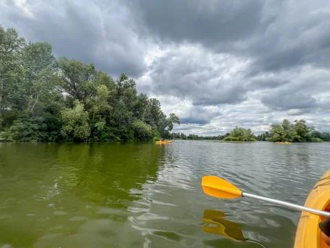 Kayaking on green river under cloudy sky with lush vegetation Stock Photos