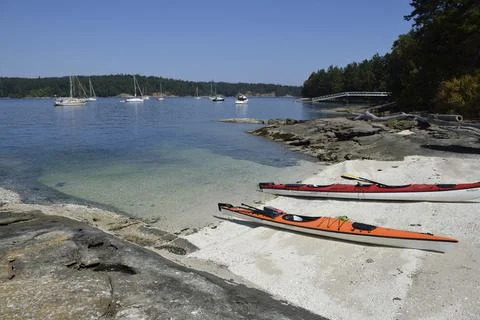Kayaks on a shell beach in front of anchored boats. Russell Island, British C Stock Photos