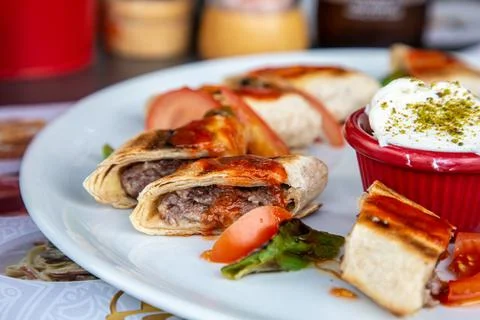Kebab wrapped in thin pita bread with tomatoes and sauce lies on a plate Stock Photos