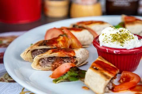 Kebab wrapped in thin pita bread with tomatoes and sauce lies on a plate Stock Photos
