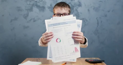 Keen boy happily presents sheets jotting down notes at desk Stockbeeldmateriaal 304363620