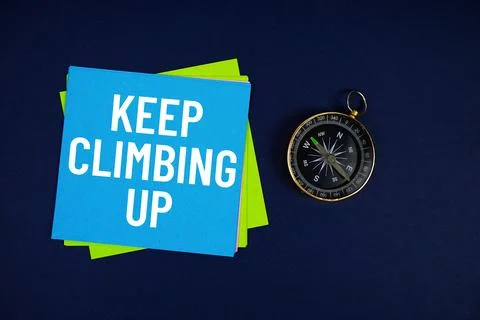 Keep Climbing Up text written on sticky note with compass on blue  background Stock Photos