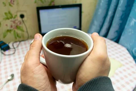 Keep a cup of tea in your hands in front of a laptop on the table at breakfas Stock Photos