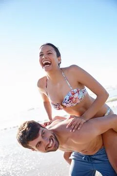 Keeping our playfulness alive. a young man giving his girlfriend a piggyback on Stock Photos