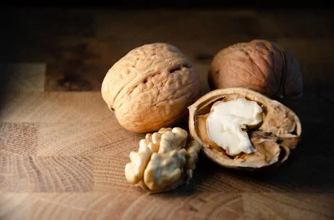 Kernel of young walnut lies next to nuts in shell on brown wooden background. Stock Photos