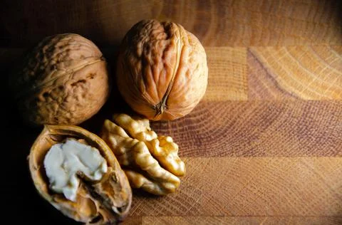 Kernel of young walnut lies next to nuts in shell on brown wooden background. Stock Photos