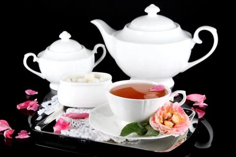Kettle and cup of tea from tea rose on metallic tray on napkin black backgrou Stock Photos