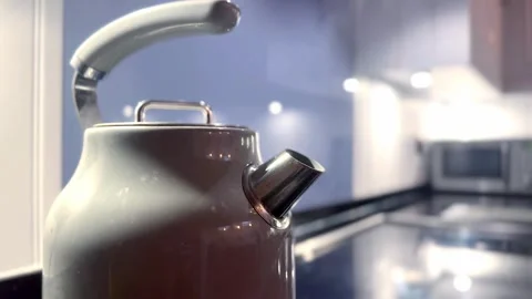 Kettle boiling with steam emerging from spout with modern kitchen background Vídeo Stock 336344026