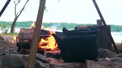 Kettle standing by the fire on a hike against the backdrop of the river Stock Footage 202717547