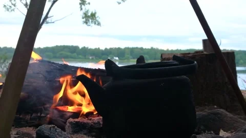 Kettle standing by the fire on a hike against the backdrop of the river Stock Footage 202717561