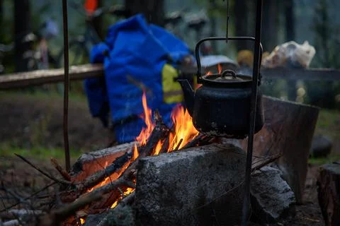 The kettle stands over a fire in the forest. A smoked kettle over the fire. Stock Photos
