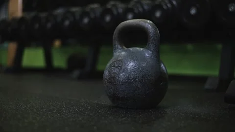 A kettlebell rests on the floor of a gym surrounded by various weights. The Vídeo Stock 345027047