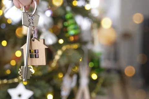 Key and tiny house keychain in hand on background fairy lights Christmas tree. 스톡 사진