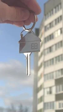Key with a keychain of a house on background of multi-storey building. Hand.. Fotos de archivo