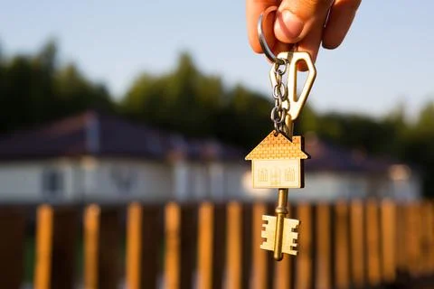 Key ring with keychain house in hand. Background of fence and cottage. Moving Foto stock