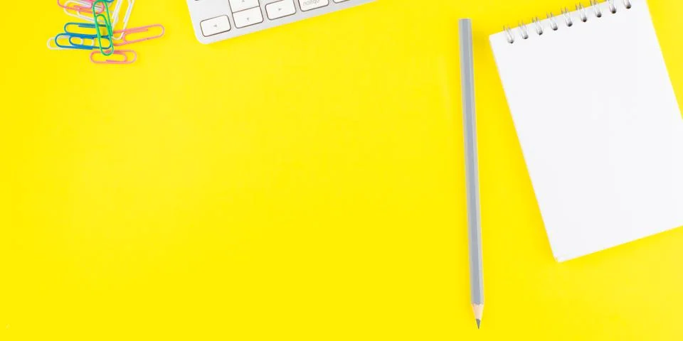Keyboard, gray pencil, notepad planner and colorful clips on yellow backgroun Stock Photos