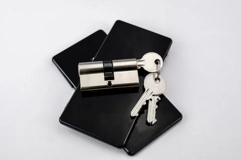 Keychain with keys inserted in a lock on two black mobile phones on white bac Stock Photos