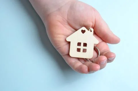 Keychain in the shape of a house in hands. Close-up. Blue background. Stock Photos