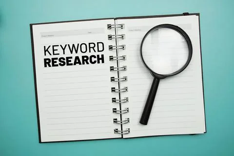 Keyword Research text on notepad and magnifying glass on blue background Stock Photos