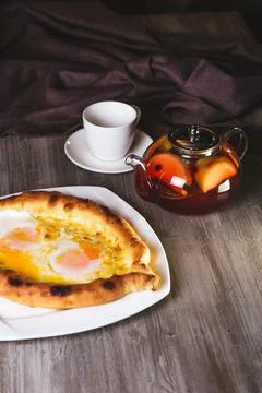 Khachapuri with egg and teapot of tea on the table Stock Photos