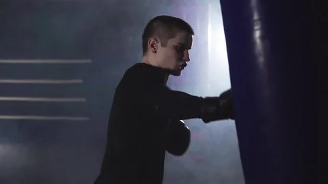 Kickboxer training with punching bag. Boxer punching in smoky studio Video stock 109792282