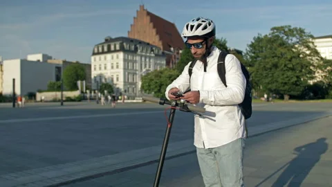 Kicksharing. Man with a backpack and in a protective helmet uses his phone to Stock Footage 220064055