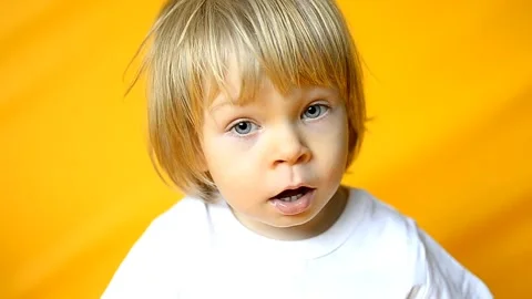 The kid is 2 years old with blonde hair, dressed in a white T-shirt and yellow Stock Footage 251555067