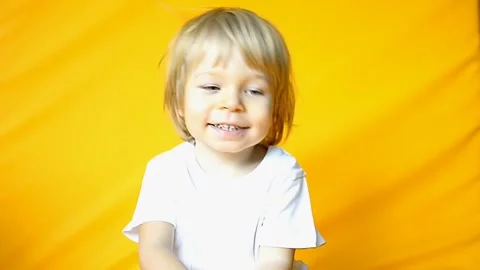 The kid is 2 years old with blonde hair, dressed in a white T-shirt and yellow Stock Footage 255100195