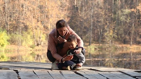 Kid and his mom using smartphone in the autumn park	 Stock Footage 124009136