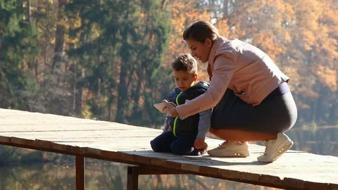 Kid and his mom using smartphone in the autumn park	 Stock Footage 124009158