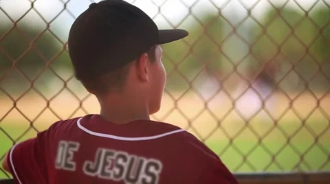 Kid in baseball uniform looking at game from behind fence Video stock 55849000