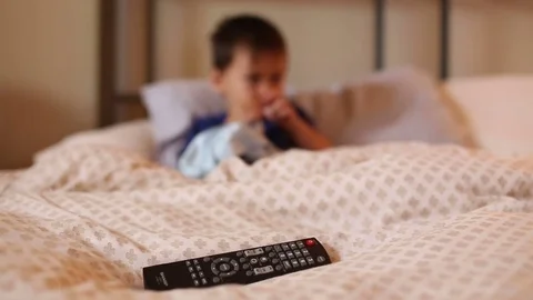 Kid in bed watching TV with remote in foreground, video Stock Footage 78547806